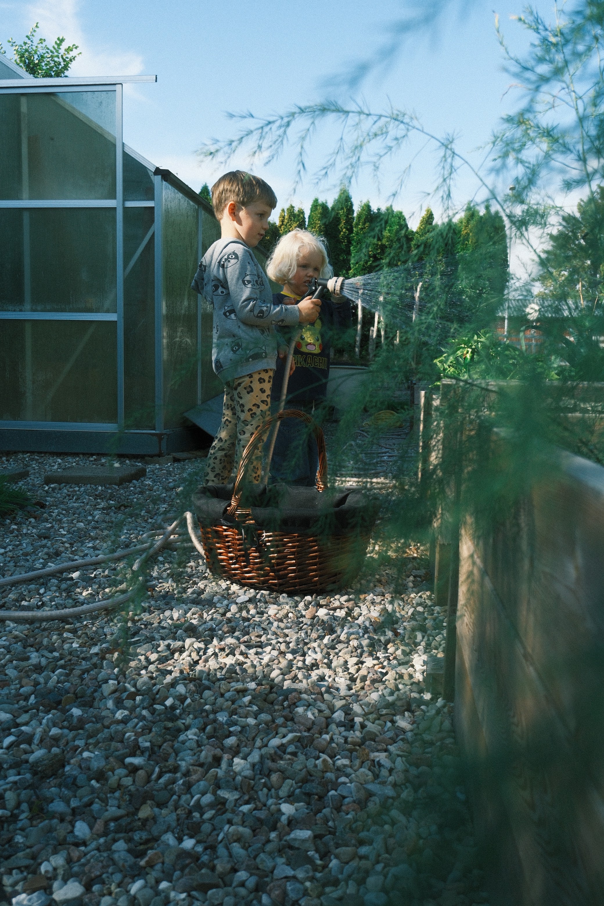 Two children watering plants together beside the greenhouse